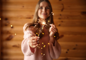 Beautiful woman with sparkler on wooden background