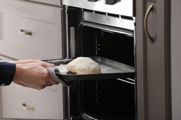 Woman putting baking tray with raw dough for bread into oven