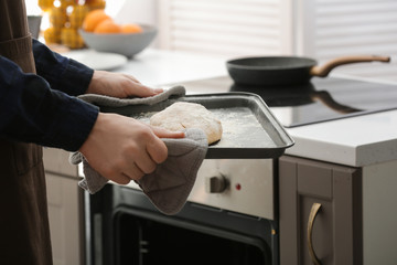 Woman holding baking tray with raw dough for bread in kitchen