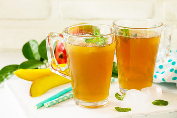 Fruit tea cups. Iced tea mango with mint on rustic white table.