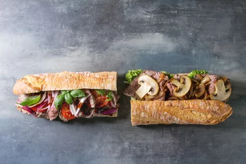 Foto op Canvas Two Beef baguette sandwiches with champignon mushrooms, green salad, fried onion, tomatoes over blue texture background. Flat lay, space © Natasha Breen