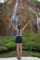 Girl standing arms outstretched doing yoga by large waterfall at Plitvice National Park Croatia