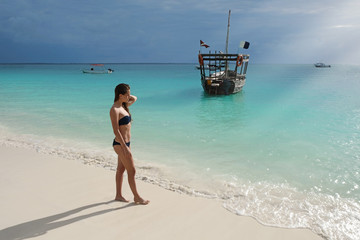 Attractive slim brown-haired woman in a bikini on a white sandy paradise beach Kendwa of Indian Ocean of Zanzibar island