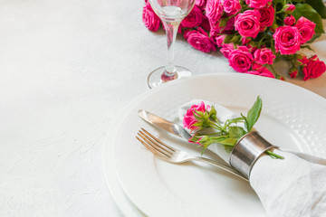 Romantic table setting with pink roses as decor, dishware, silverware, and decorations. Top view.