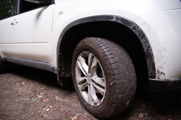 Fototapeta na wymiar white suv car at forest trail wheel in dirt close up