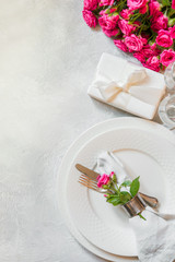 Romantic table setting with pink roses as decor, dishware, silverware, and decorations. Top view.