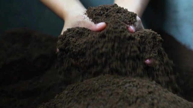Farmer hands holding and pouring black organic soil in slow motion