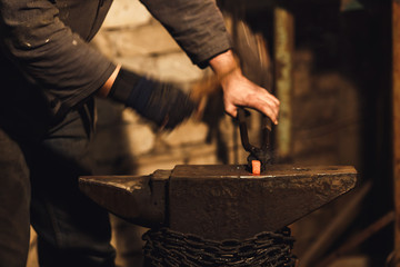 The blacksmith manually forging the red-hot metal on the anvil in smithy.