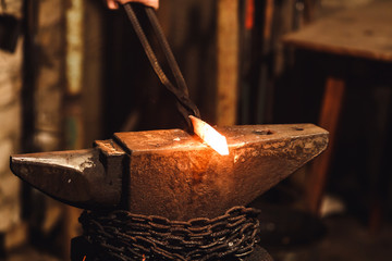 The blacksmith manually forging the red-hot metal on the anvil in smithy.