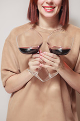 Redhaired girl sommelier on white background and hold with two glasses of red wine. Concept alcoholism, alcohol addiction, bad habit, collection rare wine, blind degustation