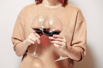 Redhaired girl sommelier on white background and hold with two glasses of red wine. Concept alcoholism, alcohol addiction, bad habit, collection rare wine, blind degustation