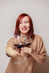 Young cheerful redhaired girl sommelier on white background smile, winks and hold with two glasses of red wine. Concept work with collection rare wines