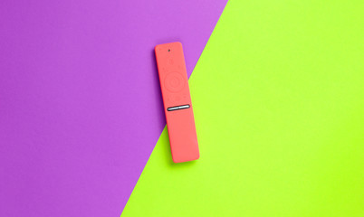 TV remote control in a red silicone case on a purple-green paper background. Minimalism, top view