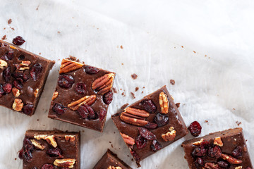 homemade chocolate fudge brownies with pecan nut and dried cranberry on white baking paper background.