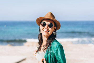 Cute pan asian girl in hat and sunglasses in green pareo walking on the seaside.