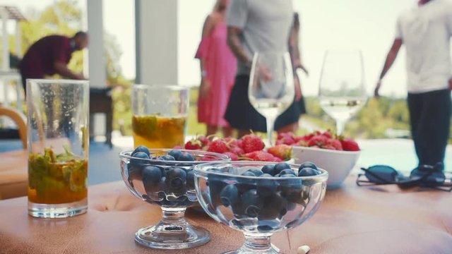 Blurred background with dancing and fun people on pool villa with view and alcohol drinks cocktails with berries on foreground