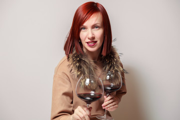 Young funny redhaired girl sommelier with fur cape on white background smile, hold two glasses red wine. Concept alcoholism, addiction, bad habit, collection great rare wines, winelover, expert