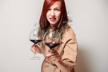 Young funny redhaired girl sommelier with fur cape on white background smile, hold two glasses red wine. Concept alcoholism, addiction, bad habit, collection great rare wines, winelover, expert