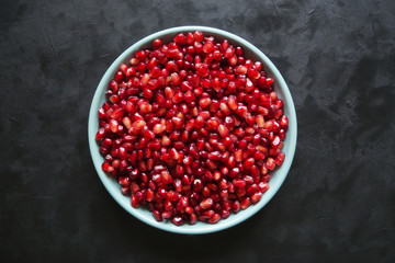 Pomegranate seeds on a plate on a black table. 