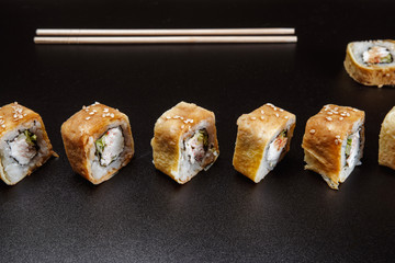 Two chopsticks, sushi and rolls on black background