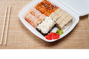 Two cTwo chopsticks, sushi and rolls in disposable packaging on wicker light background hopsticks, sushi and rolls in disposable packaging on wicker light background