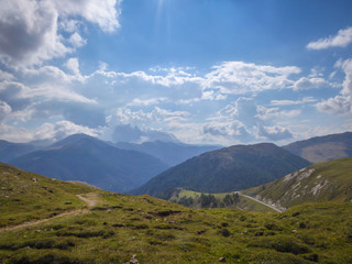 Fototapeta premium Mountain View on Carnic Alps, Austria. Endless chains of mountains, covered with clouds. Green mountain hills. Ble sky. Feeling of freedom, balance and relaxation