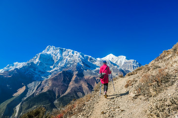 Trekkingmädchen auf dem Weg zum Eissee, Annapurna Circuit Trek, Nepal. Mädchen stützt sich auf den Trekkingstöcken ab. Trockene Trails mit kleinen Steinen darauf. Vorne hoch und schneebedeckter Himalaya-Berg.