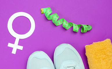 Female sport, weight loss. Training concept. Sport shoes, towel, ruller, Gender symbol feminism on a purple background. Top view