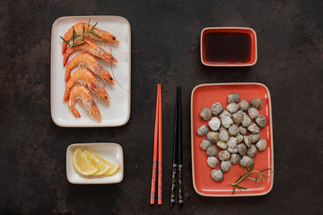 Fresh shrimps with lemon and raw Surf clam chamelea gallina  with soy sauce in Asian style with chopsticks on brown background