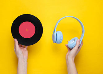 Women's hands hold over-ear headphones and vinyl record.on yellow background. Pop culture, retro...