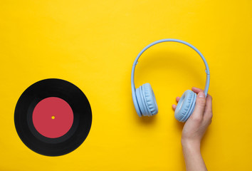 Women's hands hold over-ear headphones and vinyl record.on yellow background. Pop culture, retro style, 80s. Minimalism. Top view. Flat lay