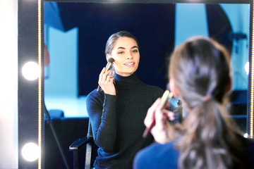 Beautiful young woman using brush while applying her makup