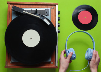 Female hands holding headphones against the background of retro vinyl record player with vinyl records on green background. Retro style. 80s. Top view