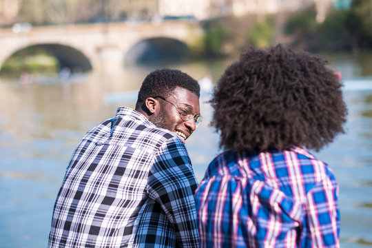 Cheerful black african couple have fun in outdoor leisure activity together near a river in the city - young man laughing with girlfriend curly afro ahir style - hipster millennial people enjoying