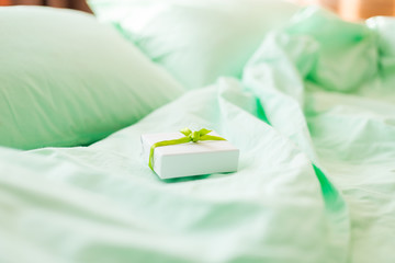 A small white gift box on minty green bed in the morning.
