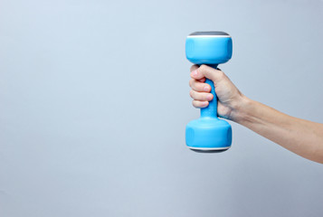 Female hand hold blue plastic dumbbells on gray background. Copy space