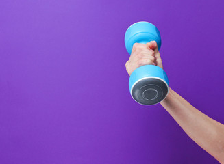 Female hand hold blue plastic dumbbells on purple background. Copy space