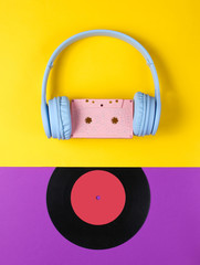 Minimalism. Headphones with audio cassette, lp record on purple-yellow background. Retro 80s. Music lover. Creative Flat lay. Top view.
