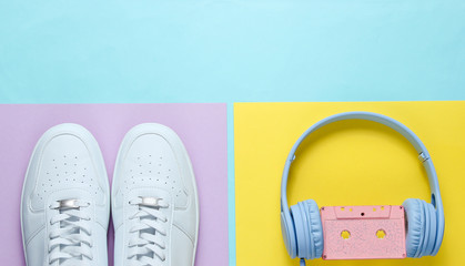 White sneakers, headphones with audio cassette. Retro 80s old fashioned objects on colore background. Top view. Flat lay.