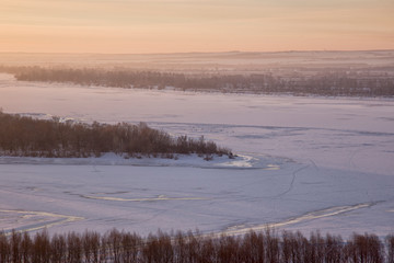 Fototapeta na wymiar Panoramic view on frozen river and forest on hill in winter during sunset from hill