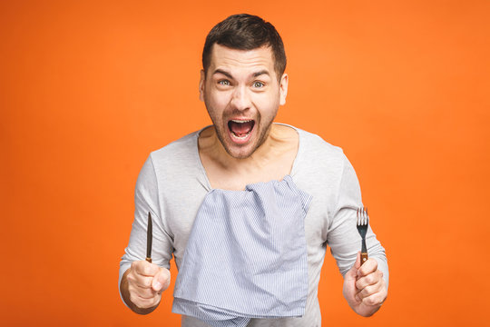 Young hungry crazy man holding a fork and a knife. Isolated on orange background.