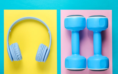 Plastic dumbbells, wireless headphones on color backgrounds. Fitness concept. Sport and music. Top view.