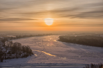 Panoramic view on frozen river and forest on hill in winter during sunset from hill