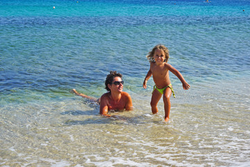 Mother and little daughter play happy in the turquoise sea of Mykonos