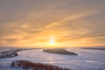 Panoramic view on frozen river and forest on hill in winter during sunset from hill