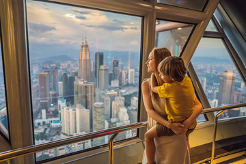 Fototapeta premium Mom and son are looking at Kuala lumpur cityscape. Panoramic view of Kuala Lumpur city skyline evening at sunset skyscrapers building in Malaysia. Traveling with kids concept