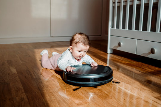 A baby with a robotic vacuum cleaner on the floor