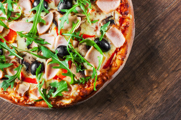 Pizza with Mozzarella cheese, mushrooms, ham, tomato sauce, pepper, olives, Spices and Fresh arugula. Italian pizza on wooden table background