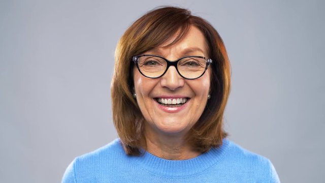 emotion, age and people concept - portrait of happy senior woman in glasses over grey background