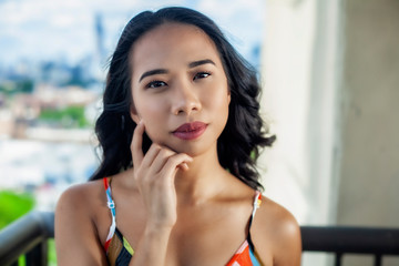 young beautiful asian woman with long black hair and dress stands outside on the balcony with the entire city view behind her